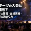 大勢の観客が集まるダーツ大会の会場で、ステージ上の選手がダーツを投げる様子とPDC大会の解説タイトル